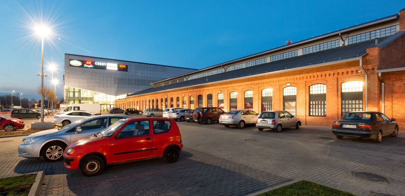 Foto: FERIO Wawer: eine historische Werkshalle mit Backsteinfassade führt zu einem Neubau; davor parkende Autos