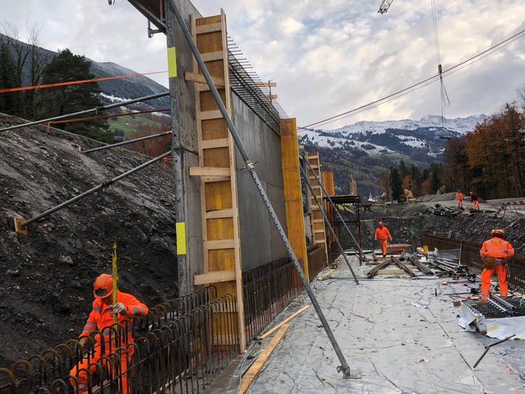 Photo: several workers on the construction site; concrete walls of the emergency access road built on the slope side.