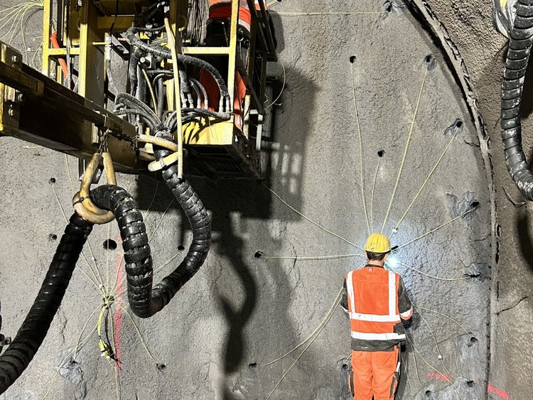 Mitarbeitende in Schutzkleidung befestigen Zündschnüre an der Tunnelwand. Einer steht am Boden, ein zweiter auf einer Hebebühne