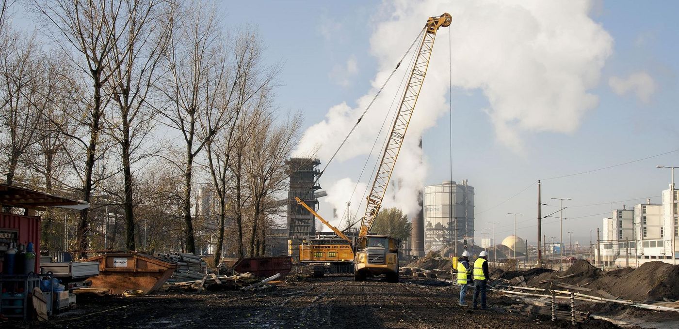 Foto: Kokerei Linz: Blick auf die Sanierungsfläche; im Vordergrund zwei Arbeiter, im Hintergrund ein großer Baggerkran 