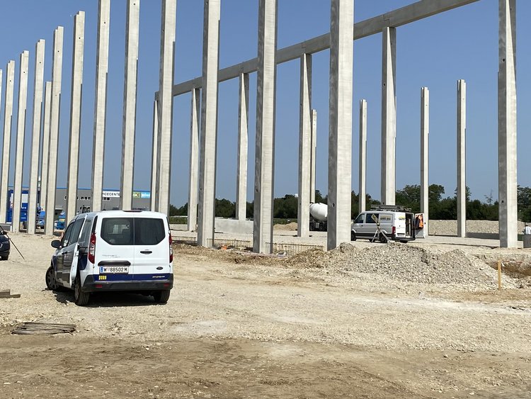 Building site with first pillars for the construction of a hall, on the right in the picture various building materials, next to it is a car, on the right in the picture other construction vehicles