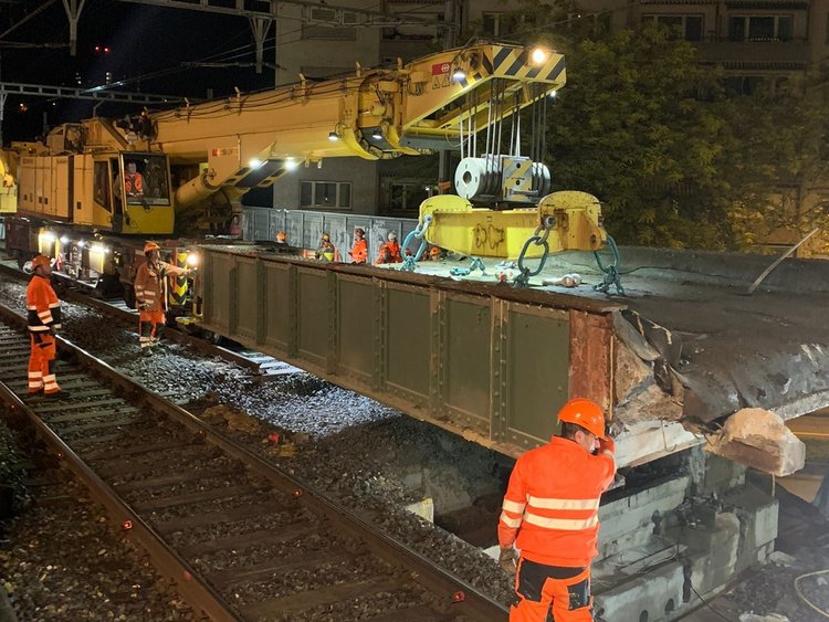 Photo: The old bridge element is lifted with a crane. The employees in orange uniforms stand on the tracks and watch the procedure.