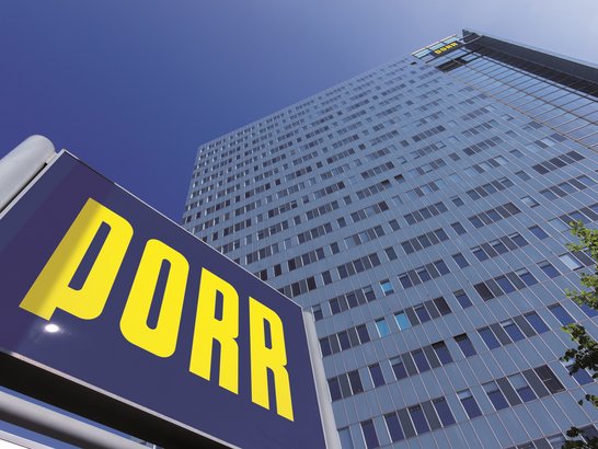 A high-rise building against a blue sky, with the blue PORR logo in the foreground