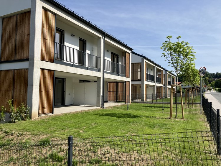 Zweistöckiger Neubau mit Holzelementen sowie Balkon und Gartenfläche.