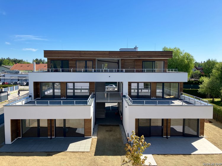Three-storey residential complex with a white façade and wooden elements, as well as large front terraces.