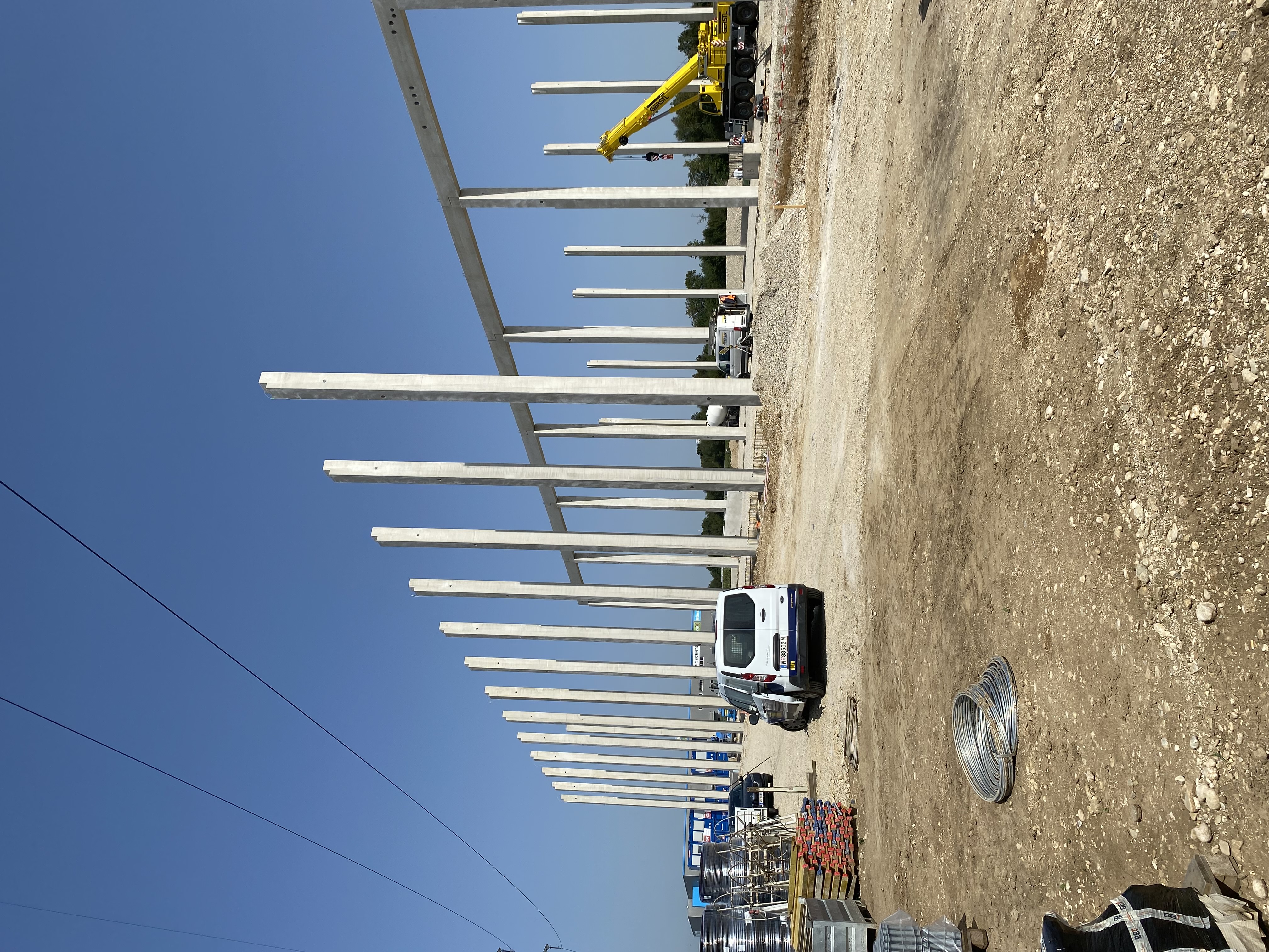 Building site with first pillars for the construction of a hall, on the right in the picture various building materials, next to it is a car, on the right in the picture other construction vehicles