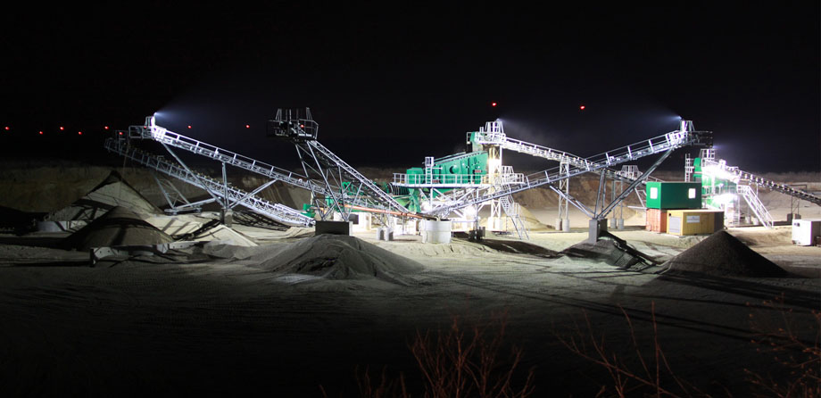 Photo: Nocturnal view of conveyor belts and heaps of gravel, illuminated by spotlights